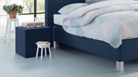 een bed met een blauw hoofdeinde en een witte kruk