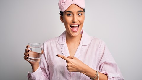 Een vrouw die een roze slaapmasker draagt die naar een glas water wijst