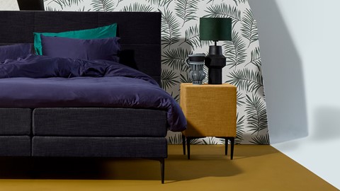 een bed met een paarse deken en een groene lamp op een tafel