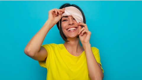 een vrouw die een geel shirt draagt en een slaapmasker over haar ogen houdt