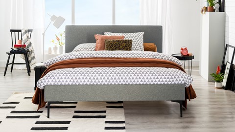 een bed met een grijs hoofdeinde en bruine kussens