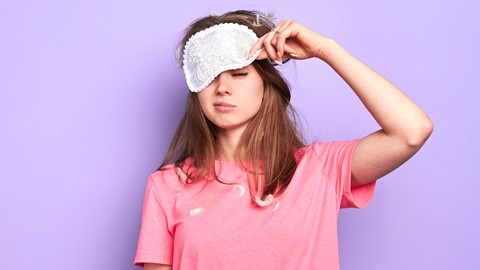 Een vrouw die een roze shirt draagt en een wit oogmasker vasthoudt