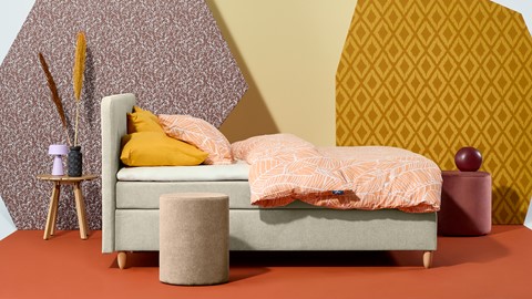 een bed met oranje kussens en een rond krukje