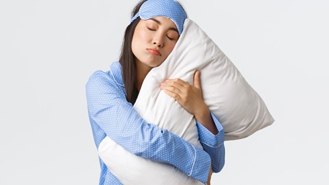 Een vrouw in pyjama die een kussen houdt