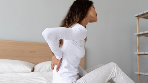 Een vrouw die op een bed zit en haar rug vasthoudt